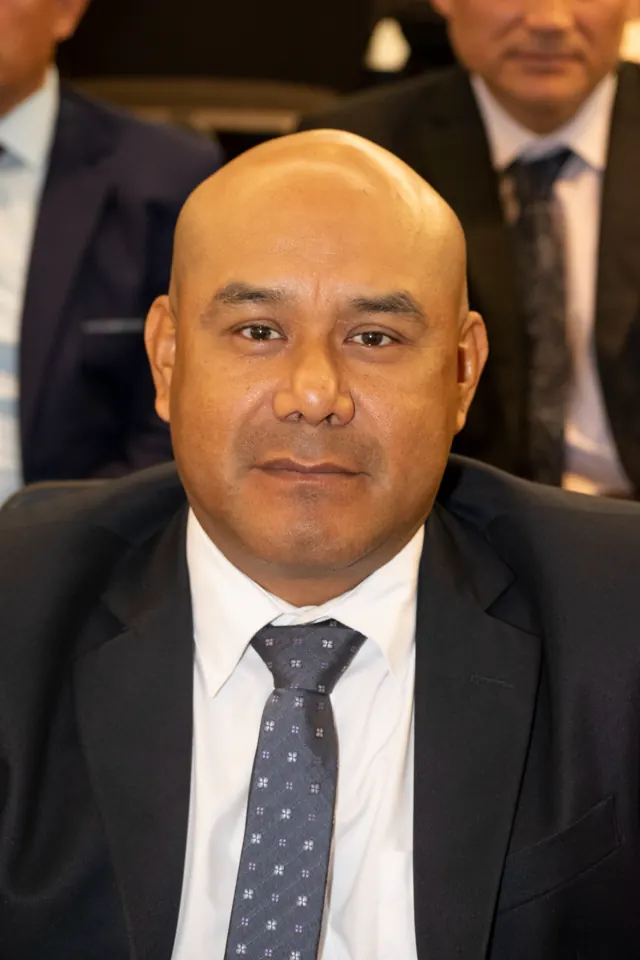 Retrato de un asistente con traje oscuro y corbata durante la ceremonia de titulación.