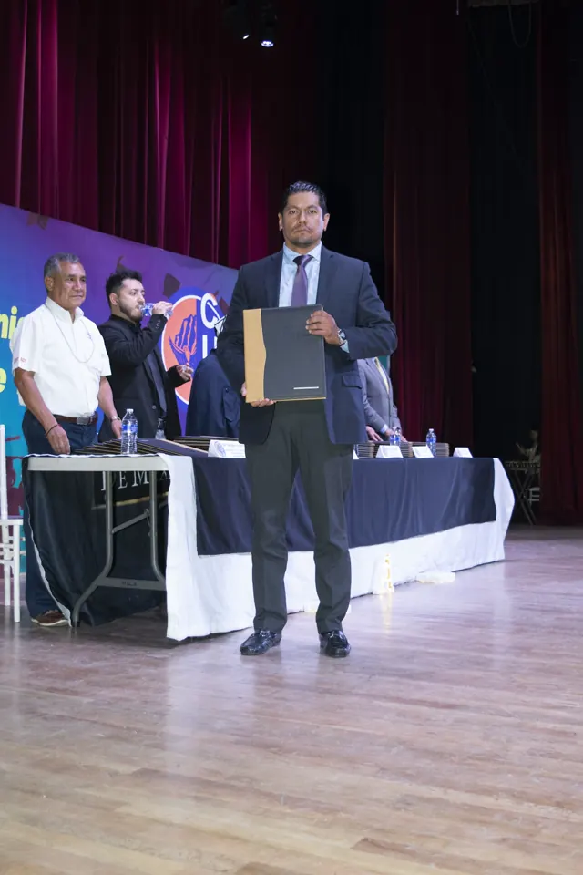 Graduado posa con su documento en el escenario. Graduación del 7 de julio de 2025.