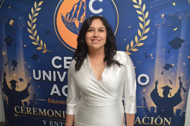 Participante sonriente con vestido blanco frente al fondo de la ceremonia de graduación.