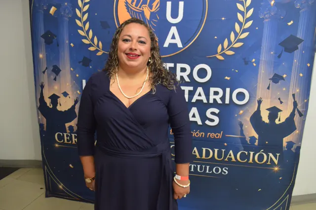 Participante sonriente con vestido azul marino posa ante el fondo de la graduación.