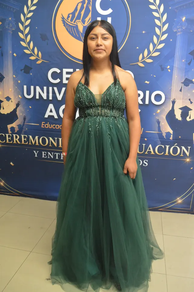 Participante con vestido largo verde posa frente al logotipo del Centro Universitario Acacias.