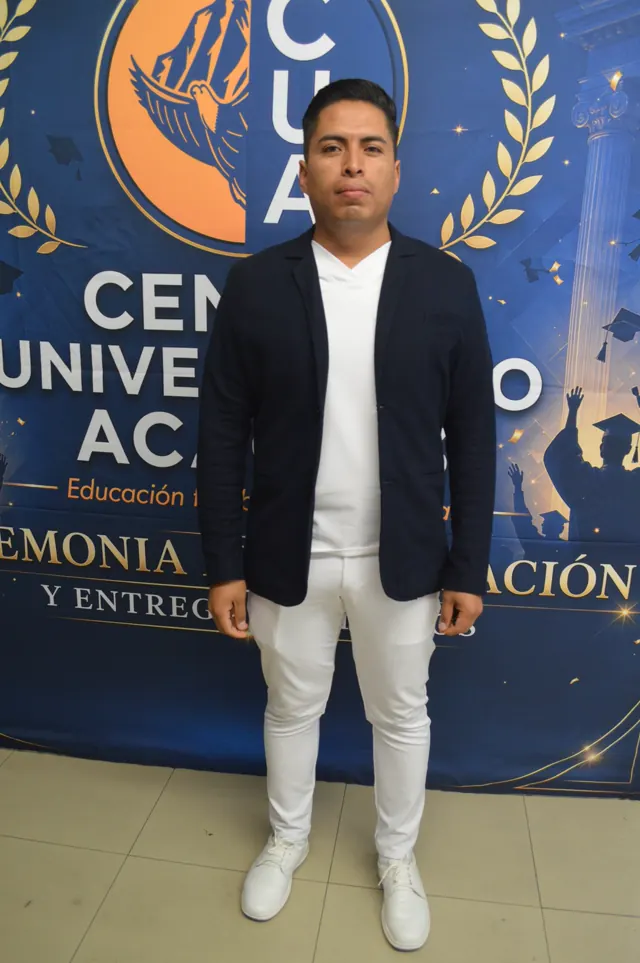 Participante con saco azul marino y pantalón blanco posa ante el fondo de la graduación.
